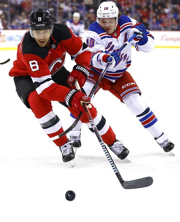 New Jersey Devils defenseman Johnathan Kovacevic (8) plays the puck against New York Rangers left wing Artemi Panarin (10) during the first period of an NHL hockey game, Monday, Dec. 23, 2024, in Newark, N.J. (AP Photo/Noah K. Murray)