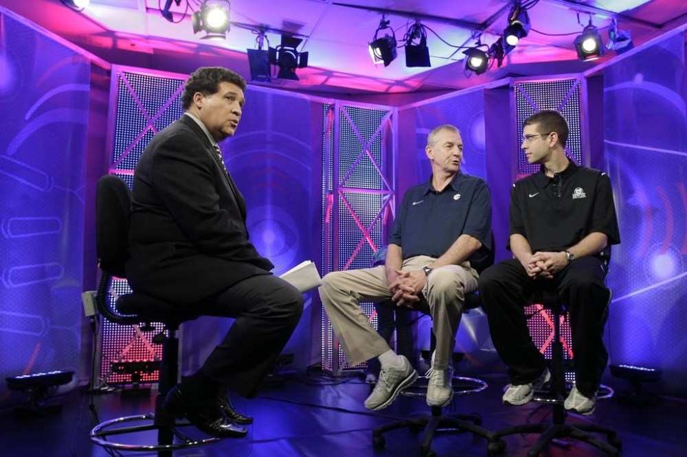 FILE - Greg Gumbel, left, watches as Connecticut head coach Jim Calhoun talks to Butler head coach Brad Stevens, right, prior to taping a television interview for the men's NCAA Final Four college basketball championship game Sunday, April 3, 2011, in Houston. (AP Photo/Eric Gay, File)