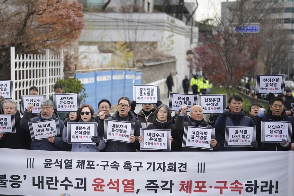 FILE - Members of civic groups shout slogans during a news conference demanding the arrest of President Yoon Suk Yeol near the presidential residence in Seoul, South Korea, on Dec. 17, 2024. The letters read