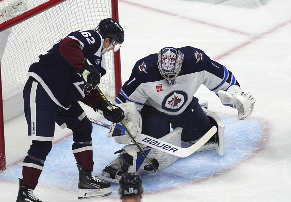 Winnipeg Jets goaltender Eric Comrie, right, stops a redirected shot by Colorado Avalanche left wing Artturi Lehkonen in the first period of an NHL hockey game Tuesday, Dec. 31, 2024, in Denver. (AP Photo/David Zalubowski)