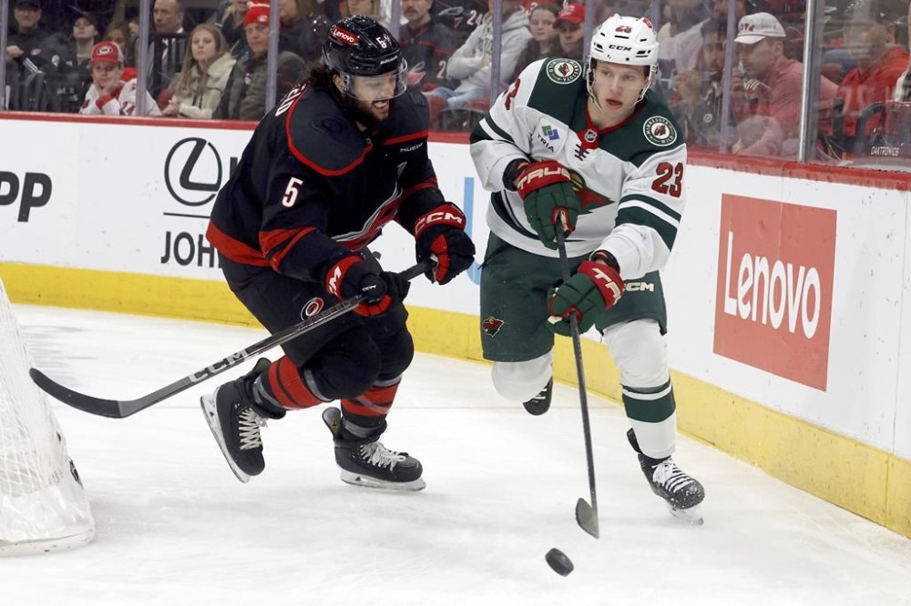 Minnesota Wild's Marco Rossi (23) controls the puck with Carolina Hurricanes' Jalen Chatfield (5) nearby during the first period of an NHL hockey game in Raleigh, N.C., Saturday, Jan. 4, 2025. THE CANADIAN PRESS/AP-Karl DeBlaker