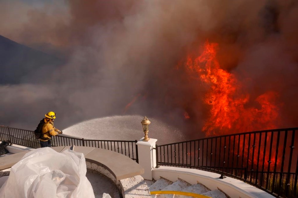 A firefighter makes a stand in front of the advancing Palisades Fire in the Pacific Palisades neighborhood of Los Angeles, Tuesday, Jan. 7, 2025. (AP Photo/Etienne Laurent)