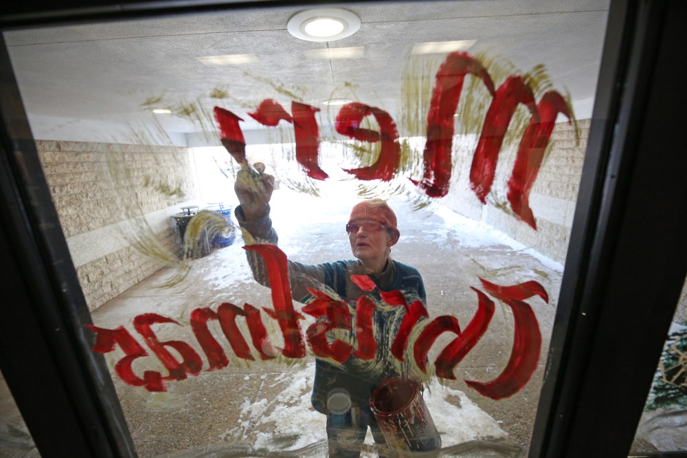Crocus Plains Regional Secondary School painting instructor Anne Boychuk paints out the letters Merry Christmas on the middle window of the high school front doors on Friday morning. At least half a dozen students from the painting class she teaches at Crocus Plains joined her to add a touch of festive colour to the school's entrance. (Matt Goerzen/The Brandon Sun)