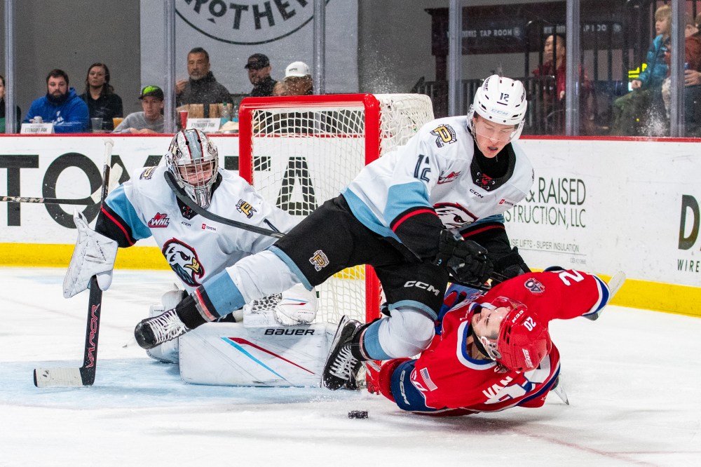 Portland Winterhawks defenceman Cole Slobodian (12) of Brandon lowers the boom on Spokane Chiefs forward Shea Van Olm as goaltender Ondrej Štěbeták (1) looks on during a game this season. (Kyle Smutzki/Portland Winterhawks)