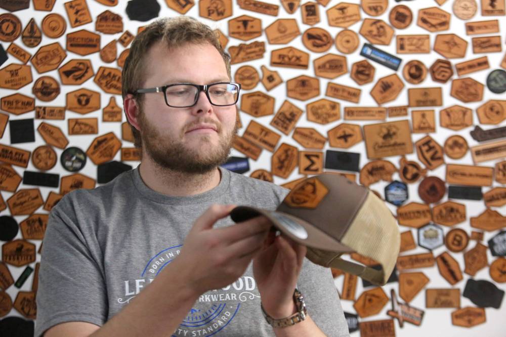 Leatherwood Custom Workwear owner Morgan James inspects one of his company’s products in front of his leather logo wall on Monday. James says the ongoing Canada Post strike has caused considerable trouble for his Brandon-based company, as nearly all of his business is conducted through the mail. (Matt Goerzen/The Brandon Sun)
