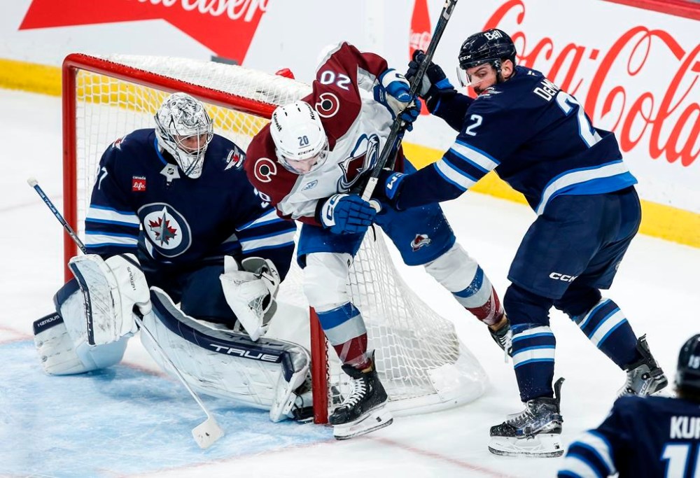 Winnipeg Jets goaltender Connor Hellebuyck (37) keeps his eye on the puck as Dylan DeMelo (2) defends against Colorado Avalanche's Ross Colton (20) during third period NHL action in Winnipeg on Saturday, January 11, 2025. THE CANADIAN PRESS/John Woods