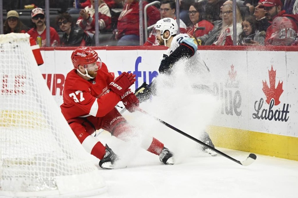 Seattle Kraken right wing Oliver Bjorkstrand, right, passes the puck in front of Detroit Red Wings left wing J.T. Compher, left, during the second period of an NHL hockey game, Sunday, Jan. 12, 2025, in Detroit. (AP Photo/Jose Juarez)