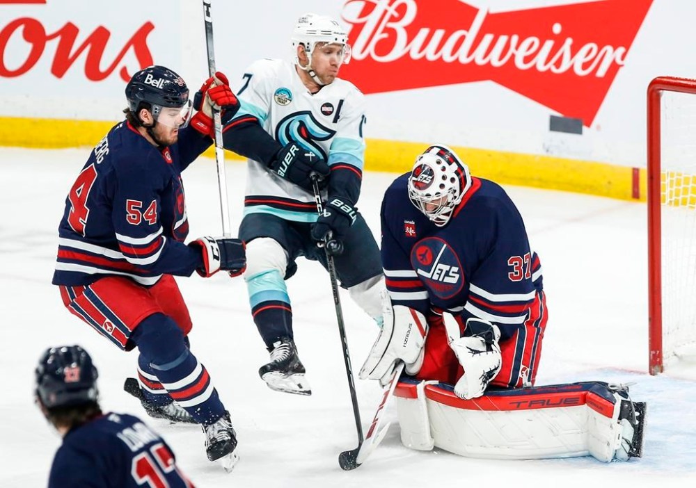 Winnipeg Jets' Dylan Samberg (54) defends against Seattle Kraken's Jaden Schwartz (17) as he tries to tip the puck past goaltender Connor Hellebuyck (37) during first period NHL action in Winnipeg on Thursday, January 16, 2025. THE CANADIAN PRESS/John Woods