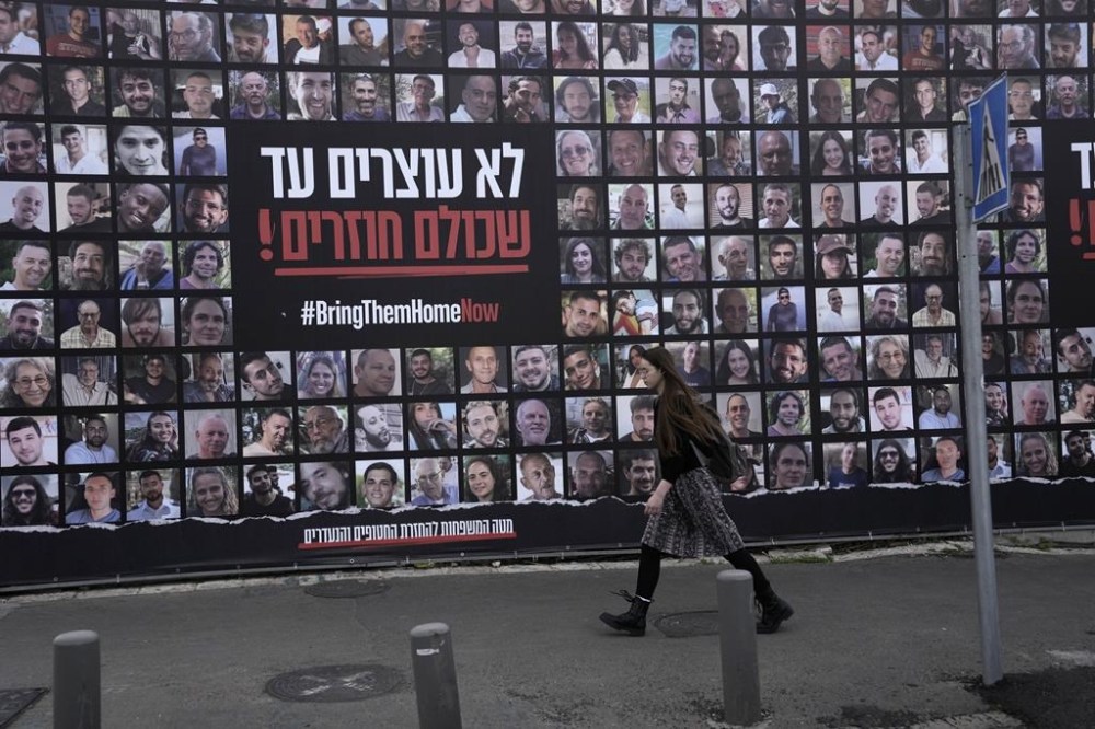 A woman walks past photos of hostages held by Hamas in the Gaza Strip, in Jerusalem, Friday, Jan. 17, 2025. (AP Photo/Mahmoud Illean)
