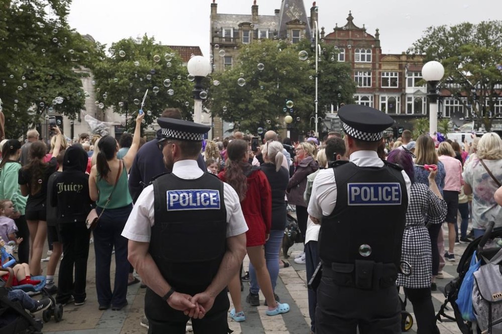 FILE - Police officers watch members of the public outside the Town Hall in Southport, England, Aug. 5, 2024 after three young girls were killed in a knife attack at a Taylor Swift-themed holiday club the week before. (AP Photo/Darren Staples, File)