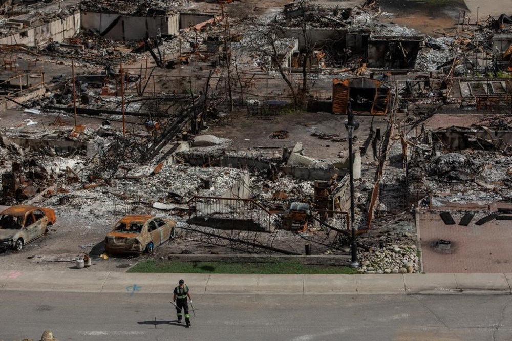A worker walks in a devastated neighbourhood in west Jasper, Alta., on Monday, Aug.19, 2024. The Municipality of Jasper says strings attached to the Alberta government's $112-million interim housing plan would mean less than half of the housing units promised months ago would actually be built in the fire-ravaged town.THE CANADIAN PRESS/Amber Bracken