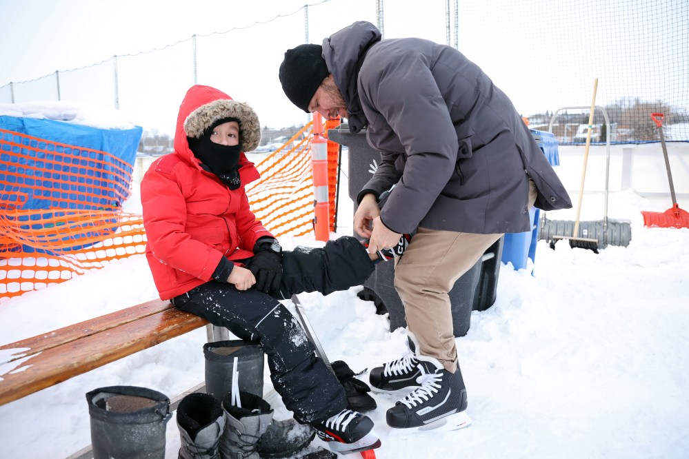 John Rincon helps his son Matteo, 7, with his skates while they enjoy the grand opening of the new North Hill Outdoor Rink at the Sportsplex Track infield on Friday afternoon. In addition to the public skate, the grand opening included a U9 hockey game between the Once Upon a Child Kings and the Precision Toyota Jets.