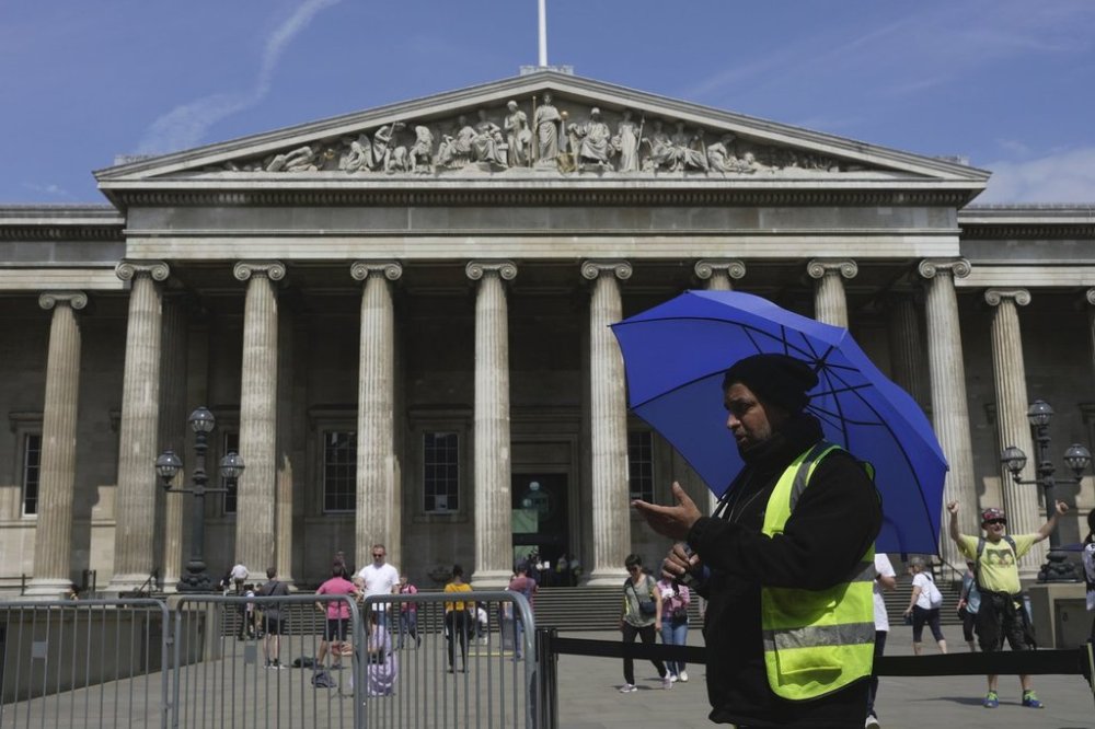 FILE - A worker holding an umbrella guides tourists at the British Museum, in Central London, Monday, June 12, 2023. (AP Photo/Kin Cheung, File)