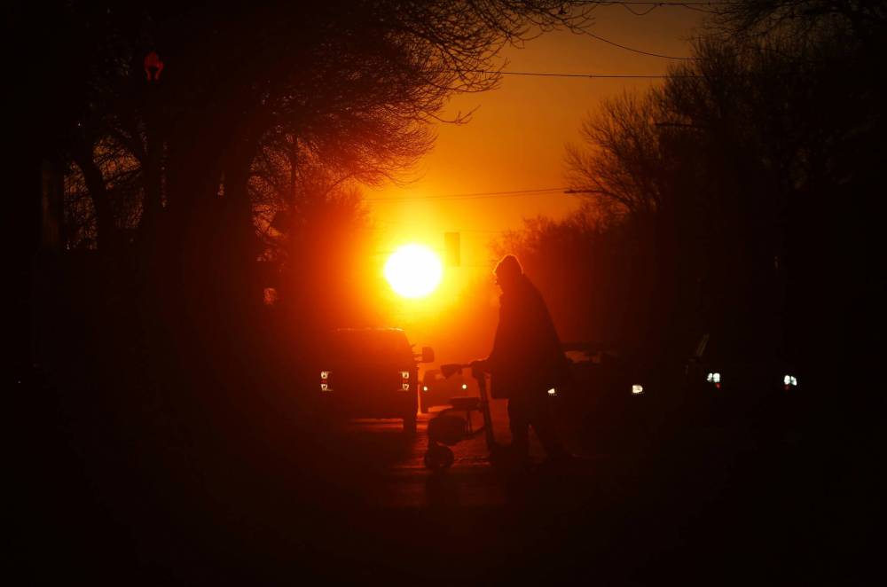 Silhouetted against the rising sun on the first day of the spring equinox in March, motorists wait at a stop light along Princess Avenue while a man with a walker crosses the street.