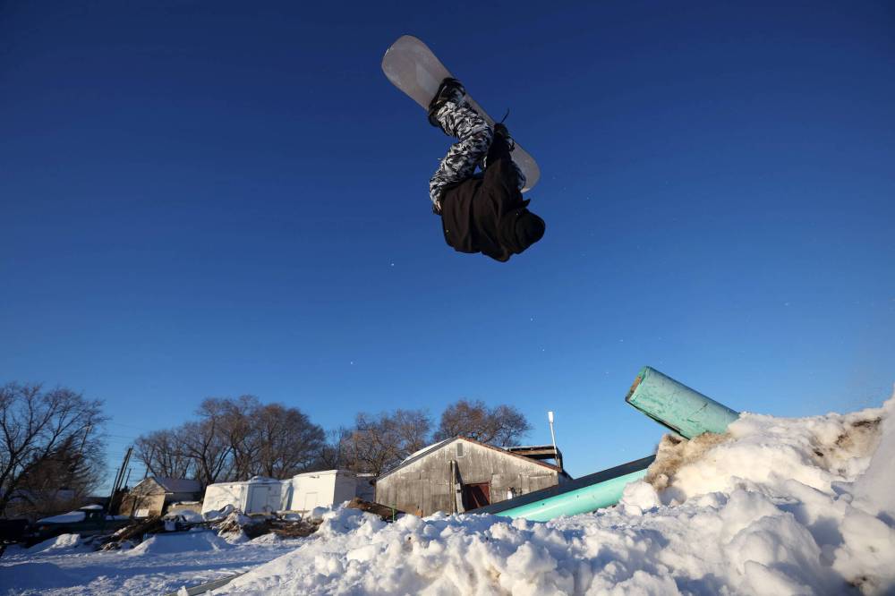 Chris Campbell backflips off a pole-jam while snowboarding in a backyard park he built with friends at his home in Brandon on a sunny and warm Wednesday afternoon.