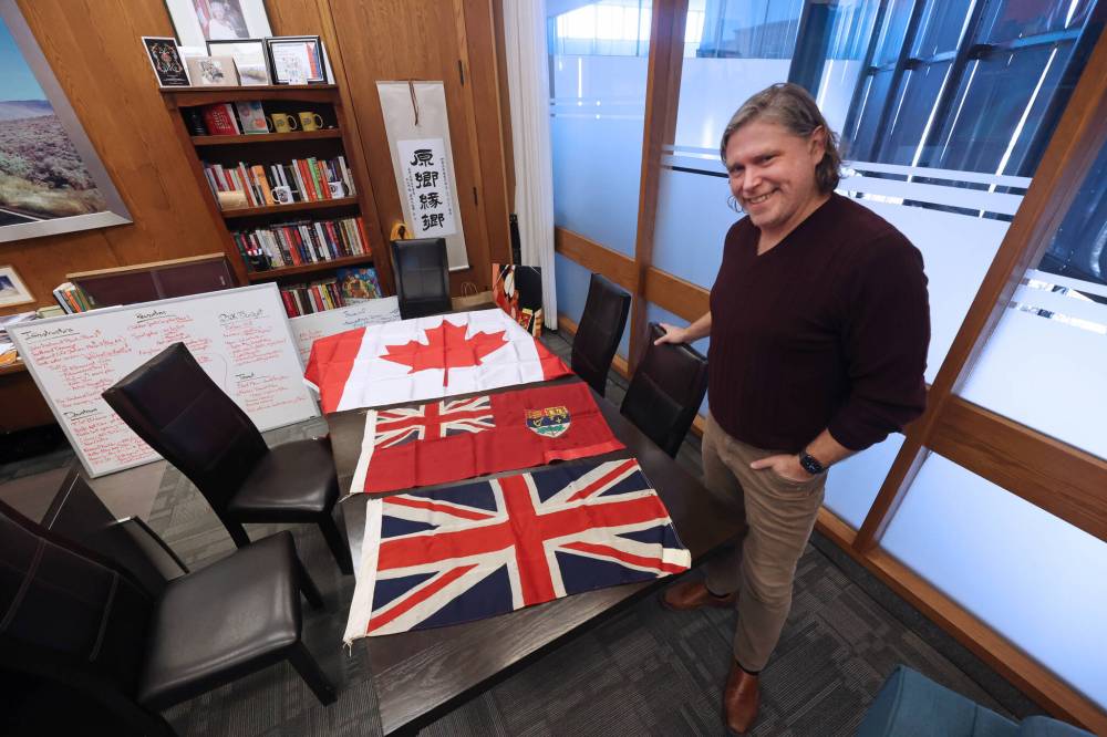 Brandon Mayor Jeff Fawcett displays a selection of flags from the city’s archives on the table in his office at city hall in advance of the 60th anniversary of the internationally recognized red Maple Leaf flag on Saturday. At the bottom of the table is the Union Jack, which was used as Canada’s national flag until 1965. The Canadian Red Ensign, which included the Union Jack and Canada’s coat of arms, was also used as a national flag until 1965. The Maple Leaf was chosen as the new national flag in 1964 and was raised on Parliament Hill on Feb. 15, 1965. The bottom two flags, which were used at local schools, now rest in the city’s archives. (Matt Goerzen/The Brandon Sun)