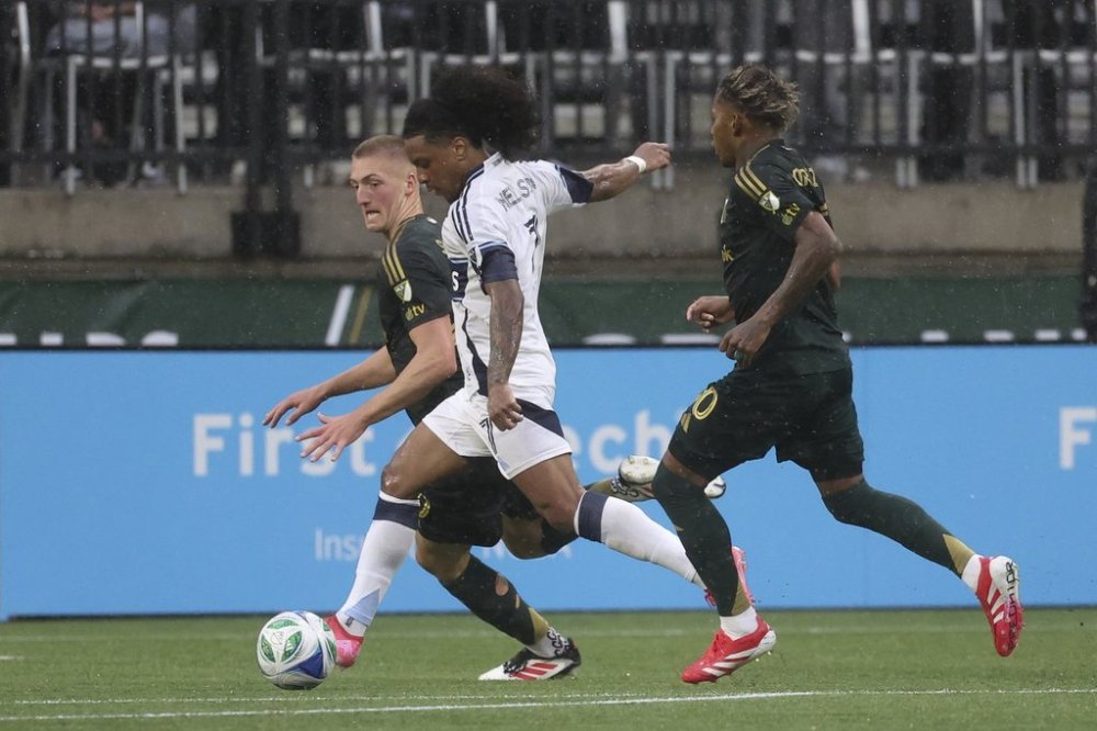 Vancouver Whitecaps forward Jayden Nelson, centre, kicks to score a goal between Portland Timbers defender Finn Surman, left, and midfielder Joao Ortiz during the second half of an MLS soccer game, Sunday, Feb. 23, 2025, in Portland, Ore. Nelson has been included in Canada's 60-man preliminary roster for the CONCACAF Nations League Finals. THE CANADIAN PRESS/AP/Amanda Loman
