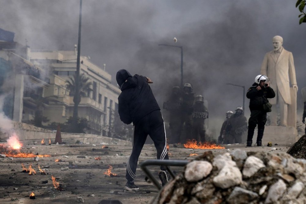 A protestor throws a stone against the riots police outside of the parliament during a rally in central Athens, Greece to mark two years since a deadly rail disaster that has also triggered hundreds of other demonstrations and a general strike, on Friday, Feb. 28, 2025. (AP Photo/Petros Giannakouris)