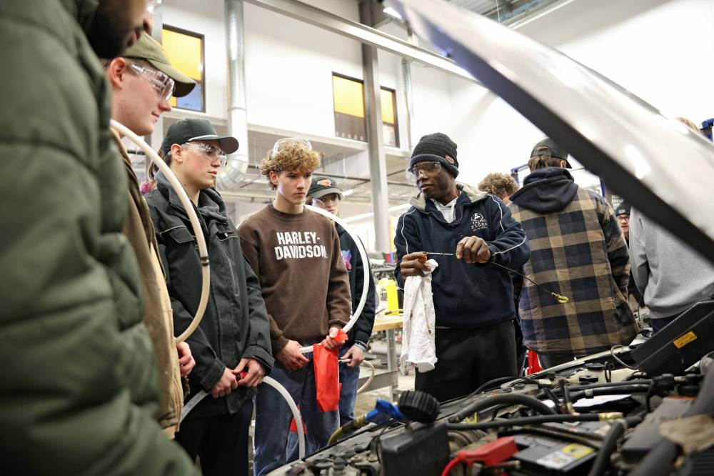 Festus Eretan, an automotive technician program student at Assiniboine College, shows students from Crocus Plains Regional Secondary School how to check the oil in a car during the Trades Summit. (Tim Smith/The Brandon Sun)
