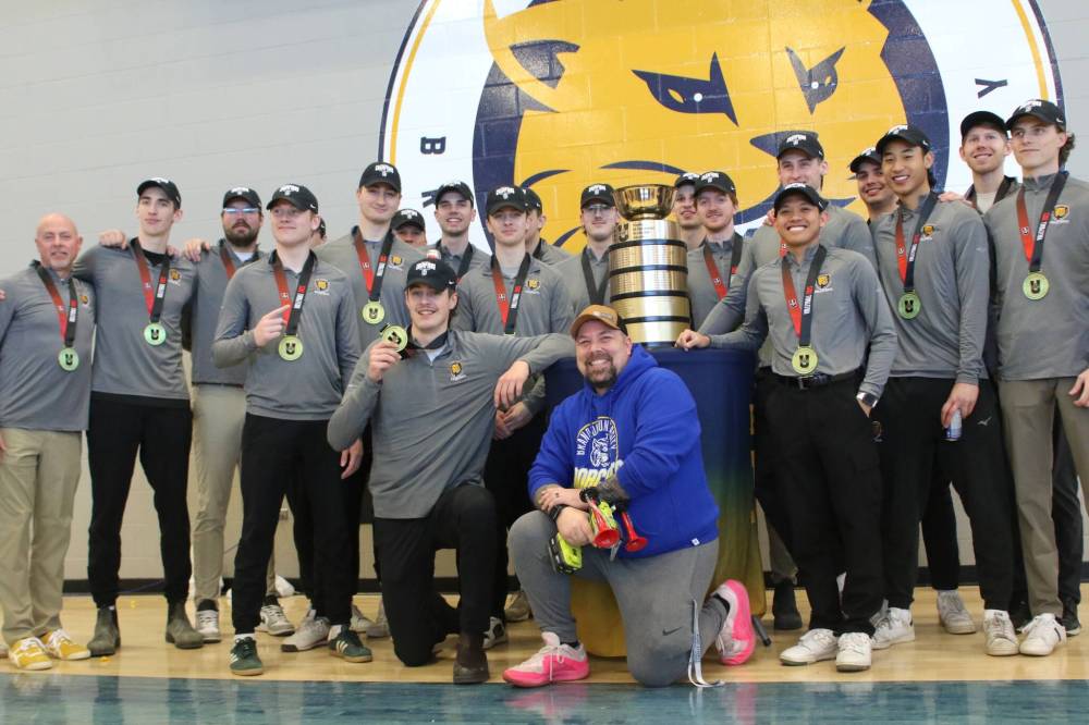 Bailey’s Cafe general manager Sean Taron kneels in front of the BU men’s volleyball team and the U Sports men’s volleyball trophy on Friday. (Thomas Friesen/The Brandon Sun)