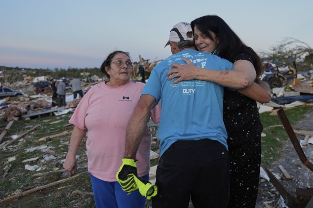 Bea Johnson, left, looks to her sister Kristie Sexton, right, as she is embraced by family friend Keith Adams as they stand next to Sexton's destroyed home after a severe storm passed through the area, Saturday, May 17, 2025, in London, Ky. (AP Photo/Carolyn Kaster)