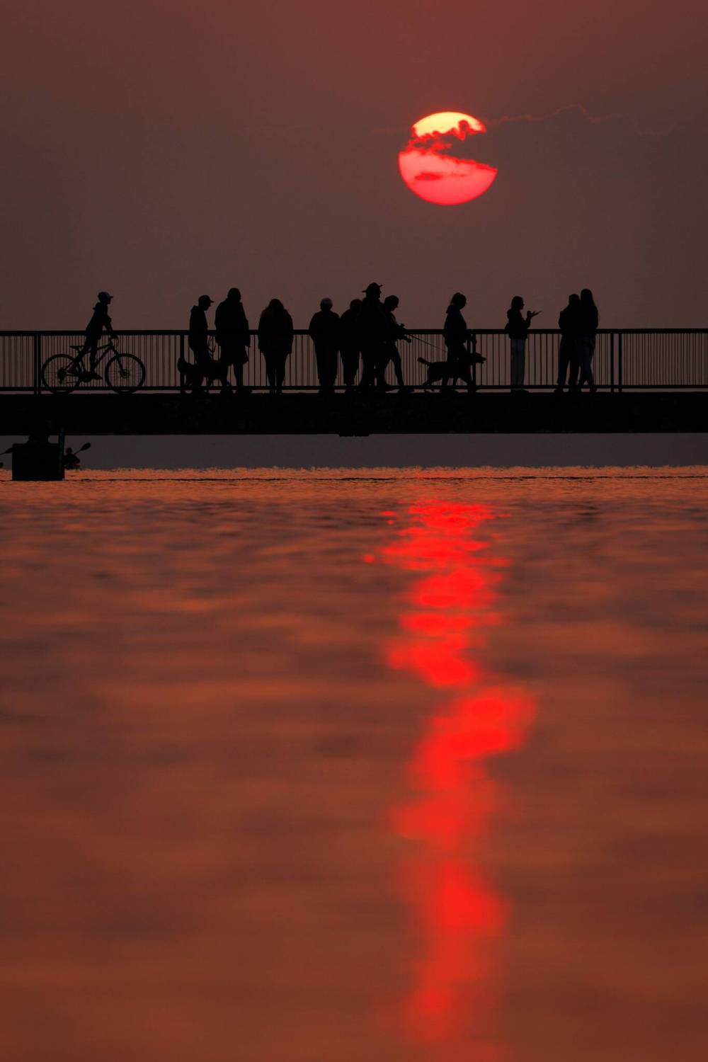 People walk back and forth or pause to take in the brilliant sunset from the Clear Lake pier at the main beach in Wasagaming on a smoky Tuesday evening. (Tim Smith/The Brandon Sun)