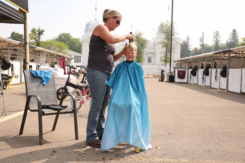 Eight-year-old Landon Hoffman has his hair cut by his mom Jenna, owner and trainer for Aerie Meadows Arabians in Minnesota, outside their stalls at the Keystone Centre on Thursday during the first day of Canada’s National Arabian Championship.