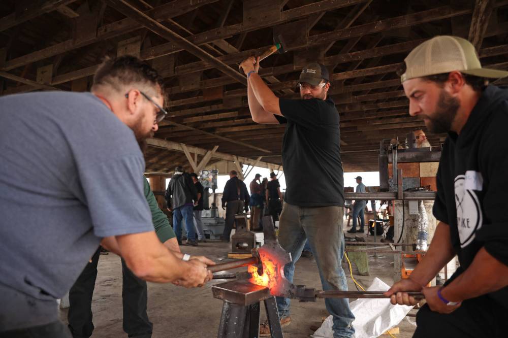 Shaun Vanbeselaere of Brunkild hammers a red-hot piece of iron while working with fellow blacksmiths on Friday.