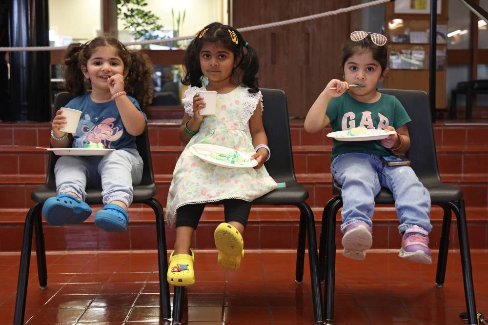 LEFT: Abeera Akram, Irha Rehman and Eliana Ahmed enjoy a piece of cake during Thursday’s celebration. RIGHT: Members of Brandon’s Pakistani community take photos as the Pakistan flag is raised on Thursday.