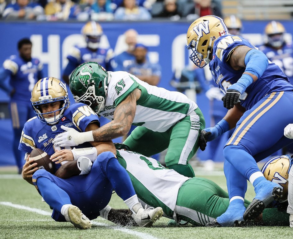 Winnipeg Blue Bombers quarterback Zach Collaros (8) gets sacked by Saskatchewan Roughriders' Malik Carney (11) and Shane Ray (5) during first half CFL action in Winnipeg, Saturday, Sept. 6, 2025. THE CANADIAN PRESS/John Woods