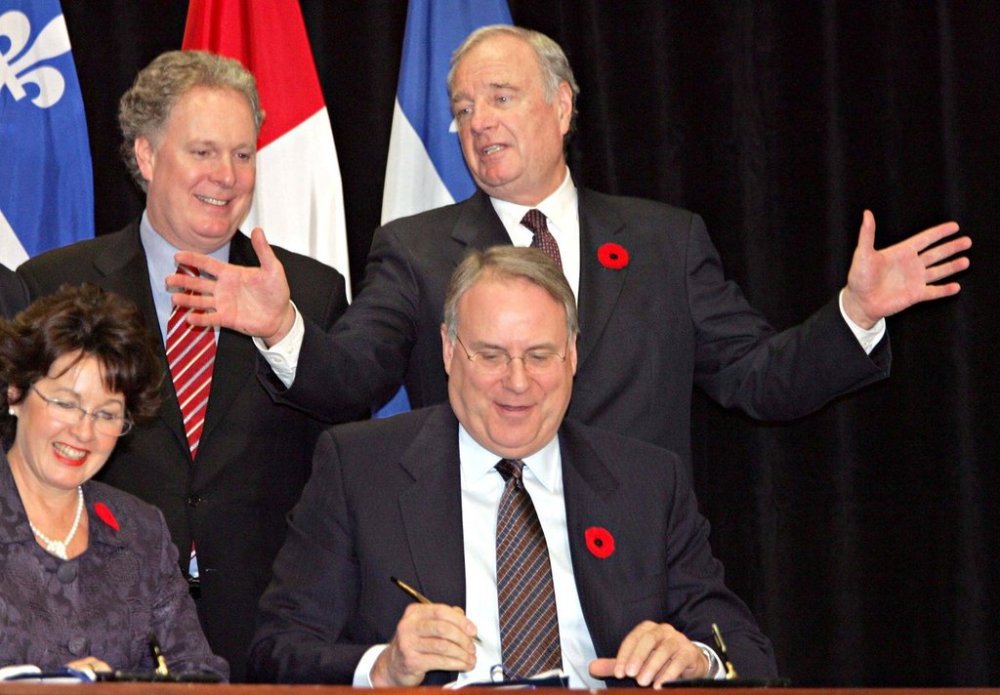Prime Minister Paul Martin gestures to Quebec Premier Jean Charest as social development Minister Ken Dryden and Carole Theberge sign a child care deal in Montreal, on Friday, Oct. 28, 2005. THE CANADIAN PRESS/Ian Barrett