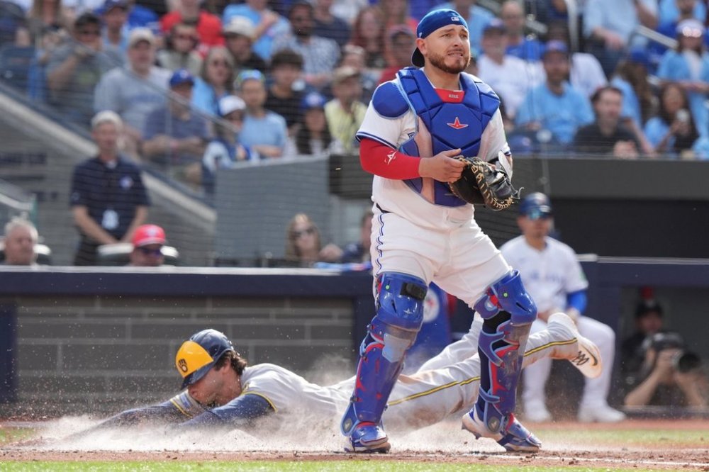 Toronto Blue Jays catcher Alejandro Kirk (30) looks for the ball as Milwaukee Brewers outfielder Christian Yelich (22) scores behind him during seventh inning MLB baseball action in Toronto on Saturday, August 30, 2025. THE CANADIAN PRESS/Frank Gunn