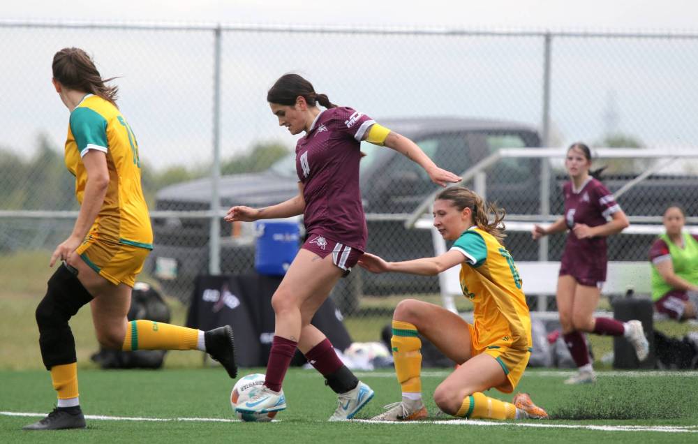Kiyanna Arevalo of the Assiniboine College Cougars dribbles through a pair of Canadian Mennonite University Blazers during their MCAC women's soccer season opener at Cougars Field on Saturday. (Thomas Friesen/The Brandon Sun)