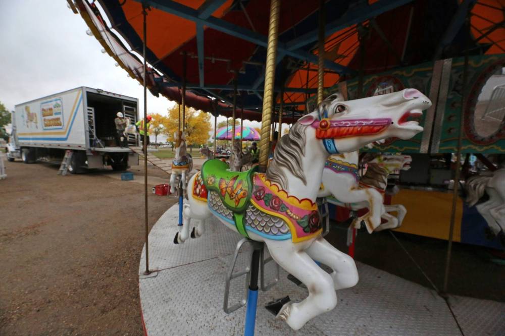 Completed carousel horses await their riders on Thursday afternoon, while a work crew with Select Shows unloads another filly in the background for this classic midway ride at the Keystone Centre grounds.