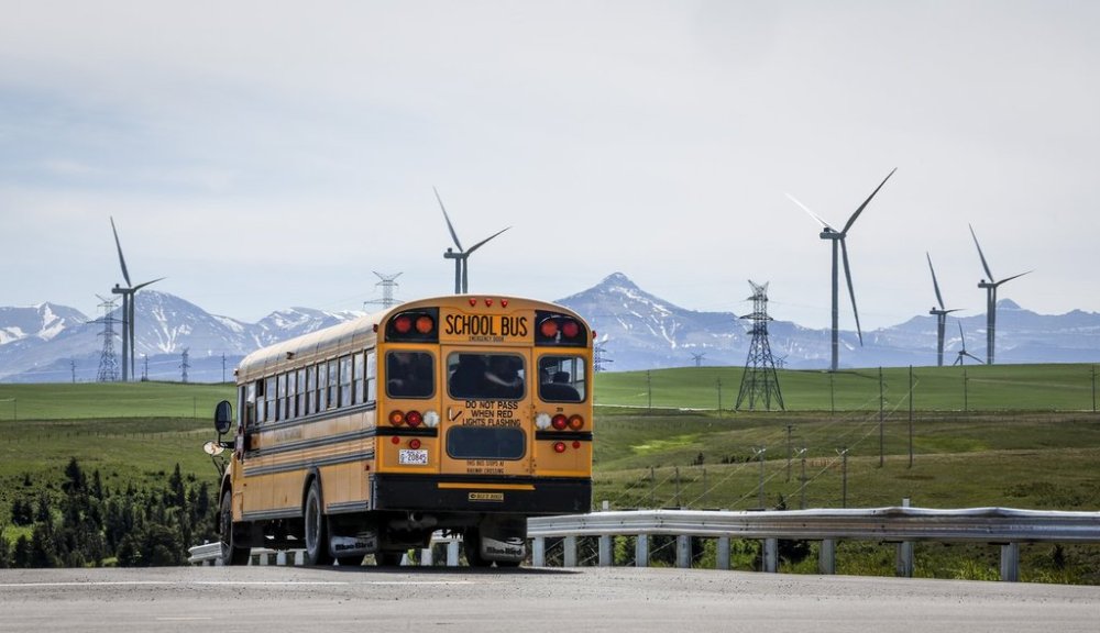 A school bus passes power transmission lines and wind turbines as seen with the Rocky Mountains in the background near Pincher Creek, Alta., Thursday, June 6, 2024. THE CANADIAN PRESS/Jeff McIntosh