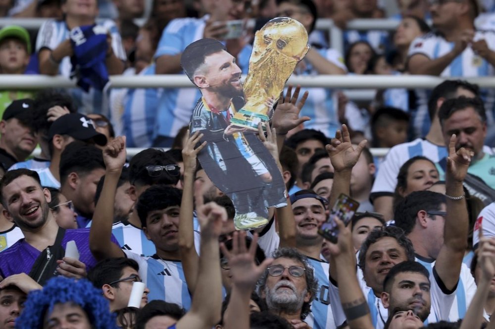 Argentina soccer fans hold a cardboard cutout with the image of soccer star Lionel Messi with the FIFA World Cup trophy as they wait for the start of an international friendly soccer match between Argentina and Curaçao in Santiago del Estero, Argentina, Tuesday, March 28, 2023. (AP Photo/Nicolas Aguilera)