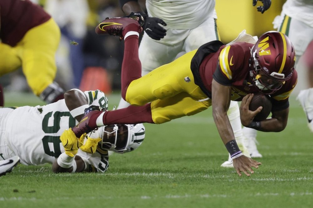 Washington Commanders quarterback Jayden Daniels, right, struggles for yardage as Green Bay Packers linebacker Isaiah McDuffie (58) defends during the first half of an NFL football game Thursday, Sept. 11, 2025, in Green Bay, Wis. (AP Photo/Matt Ludtke)