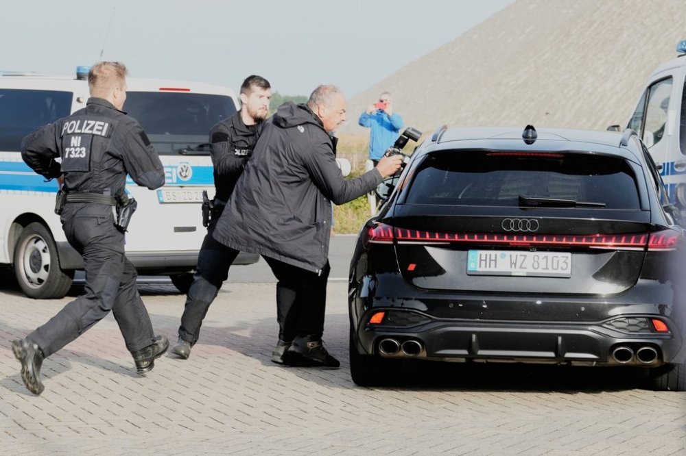 Police officers try to stop a British photographer as he takes pictures inside a car leaving a prison, carrying Christian B., a suspect in the 2007 disappearance of British toddler Madeleine McCann, in Sehnde, Germany, Wednesday, Sept. 17, 2025. (AP Photo/Markus Schreiber)