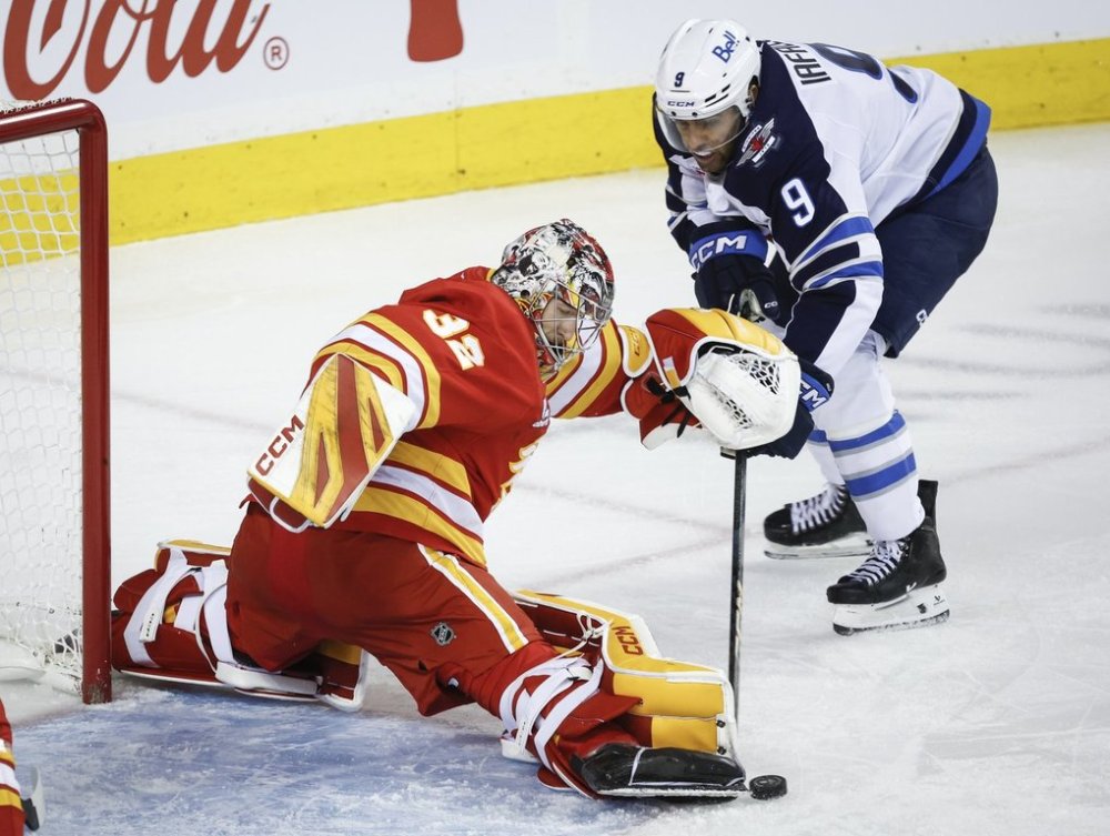 Winnipeg Jets' Alex Iafallo, right, has the puck kicked away by a stickless Calgary Flames goalie Dustin Wolf during second period NHL hockey action in Calgary, Alta., Monday, Oct. 20, 2025. THE CANADIAN PRESS/Jeff McIntosh