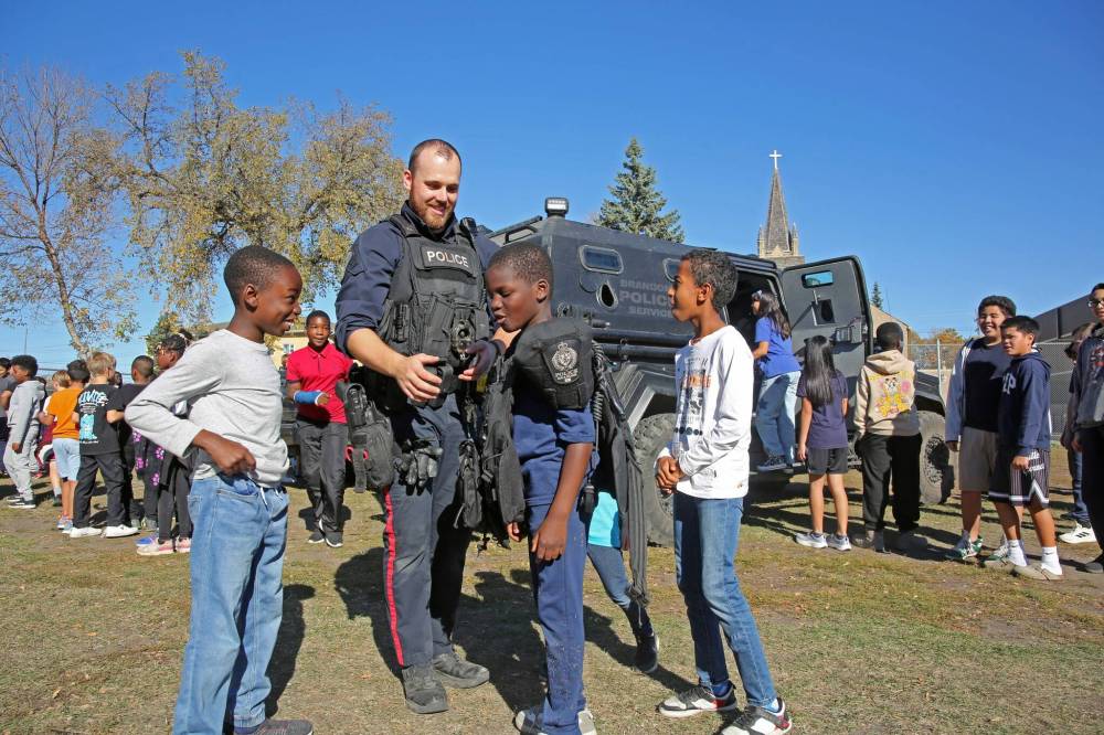 Const. Michael Dixon of the Brandon Police Service helps students try on a vest during a demonstration at St. Augustine School on Thursday. Public safety workers were brought to the school for a dedicated church service and an educational day. (Connor McDowell/The Brandon Sun)