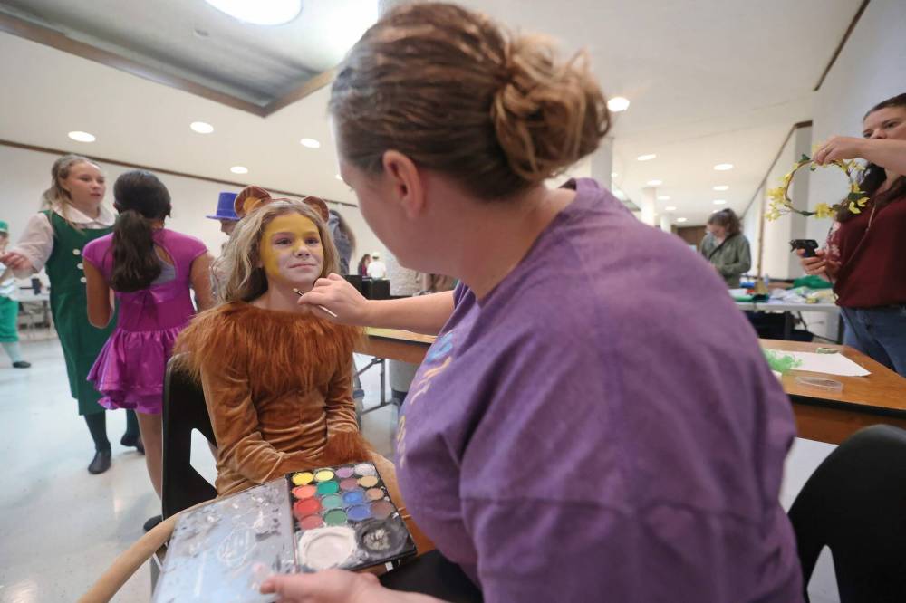 Twelve-year-old Lauren Mazer, one of two child actors playing the character of the Cowardly Lion, gets her face painted by volunteer mom Ashley Mitchel shortly before Wednesday’s dress rehearsal.