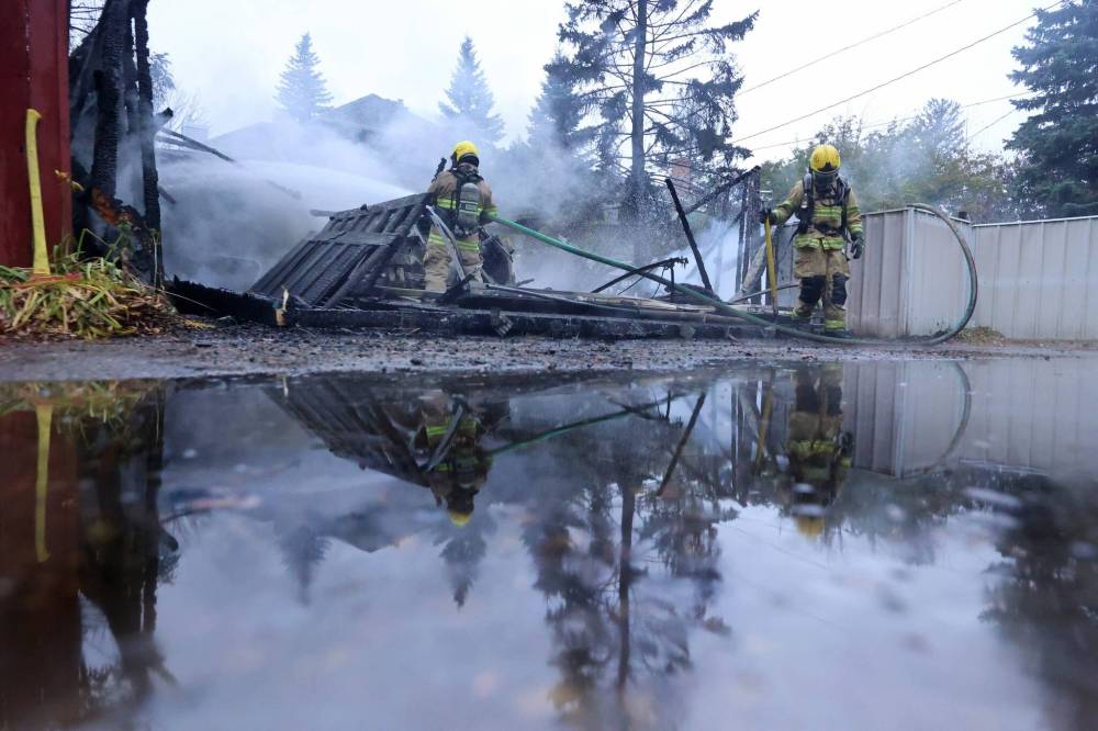 Brandon firefighters, reflected in a nearby water puddle, check for hot spots on a garage that burned down on Wednesday afternoon on the 400 block of 16th Street. Police say the fire was caused by ashes that reignited after they were placed in a pail inside the building. (Matt Goerzen/The Brandon Sun)