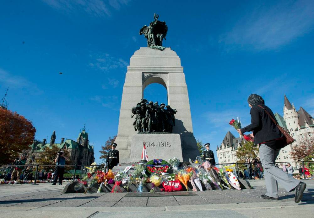People leave flowers as sentries guard the Tomb of the Unknown Soldier at the National War Memorial in Ottawa in October 2014 after Cpl. Nathan Cirillo, 24, a reservist from Hamilton, Ont., was killed while guarding the tomb by a gunman, who then moved to nearby Parliament Hill, opening fire before he himself was shot dead. (The Canadian Press)