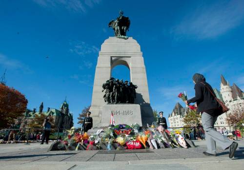 People leave flowers as sentries guard the Tomb of the Unknown Soldier at the National War Memorial in Ottawa in October 2014 after Cpl. Nathan Cirillo, 24, a reservist from Hamilton, Ont., was killed while guarding the tomb by a gunman, who then moved to nearby Parliament Hill, opening fire before he himself was shot dead. (The Canadian Press)