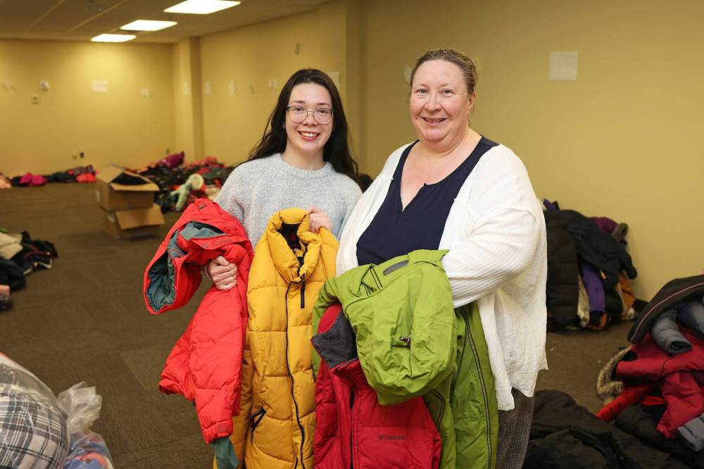 Gracie Ducharme, United Way West Central Manitoba executive assistant to the CEO, and Jamie Stouffer, director of staff development and community wellness, stand amid the many coats the organization has collected for their annual Coats for Kids and Coats for Seniors campaigns. (Tim Smith/The Brandon Sun)