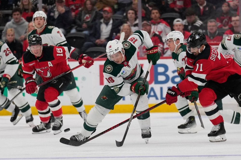 Minnesota Wild's Tyler Pitlick, center, and New Jersey Devils' Jonas Siegenthaler, right, fight for the puck during the third period of an NHL hockey game Wednesday, Oct. 22, 2025, in Newark, N.J. (AP Photo/Seth Wenig)