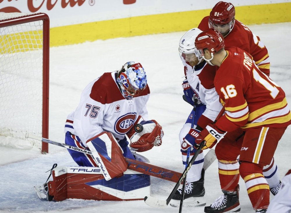 Montreal Canadiens goalie Jakub Dobes, left, grabs the puck as Mike Matheson, centre, checks Calgary Flames' Morgan Frost, front right, as Nazem Kadri, back right, looks on during first period NHL hockey action in Calgary on Wednesday, Oct. 22, 2025.THE CANADIAN PRESS/Jeff McIntosh