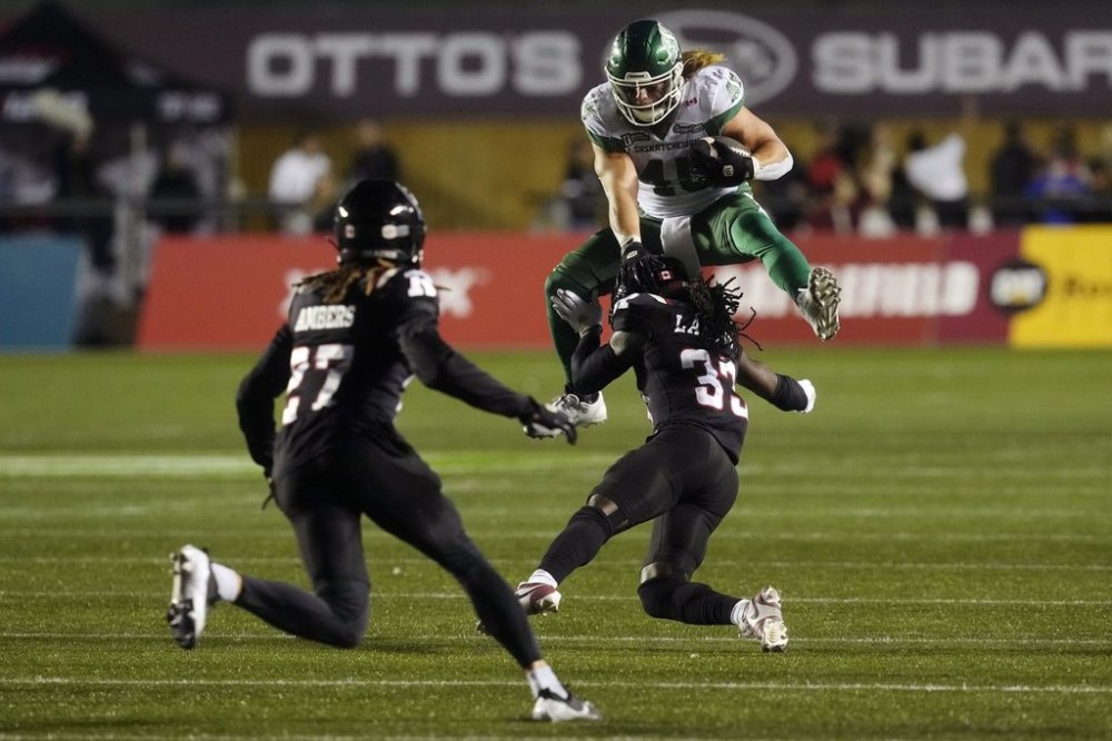 Saskatchewan Roughriders running back A.J. Ouellette (45) hurdles Ottawa Redblacks defensive back Deandre Lamont (33) as teammate defensive back King Ambers looks on during second half CFL action in Ottawa, Friday, Oct. 3, 2025. THE CANADIAN PRESS/Adrian Wyld