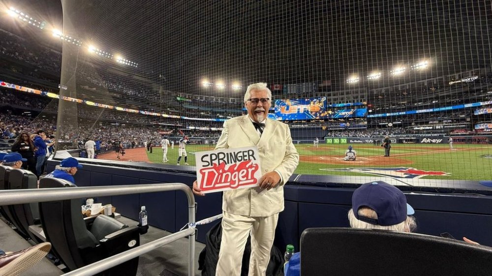 A Colonel Sanders impersonator sent by KFC Canada to promote their newly renamed sandwich, is seen in this handout photo, behind home plate at Game 2 of the World Series, in Toronto, on Saturday, Oct. 25, 2025. THE CANADIAN PRESS/Handout - KFC Canada (Mandatory Credit)
