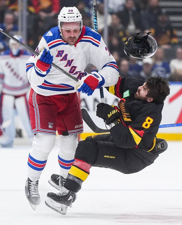 Vancouver Canucks' Conor Garland (8) loses his helmet as he's checked by New York Rangers' Sam Carrick (39) during the first period of an NHL hockey game, in Vancouver, on Tuesday, Oct. 28, 2025. THE CANADIAN PRESS/Darryl Dyck